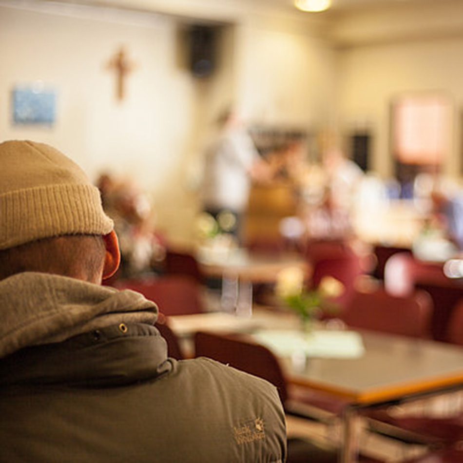Person in Mütze sitzt in Gemeinschaftsraum mit Tisch