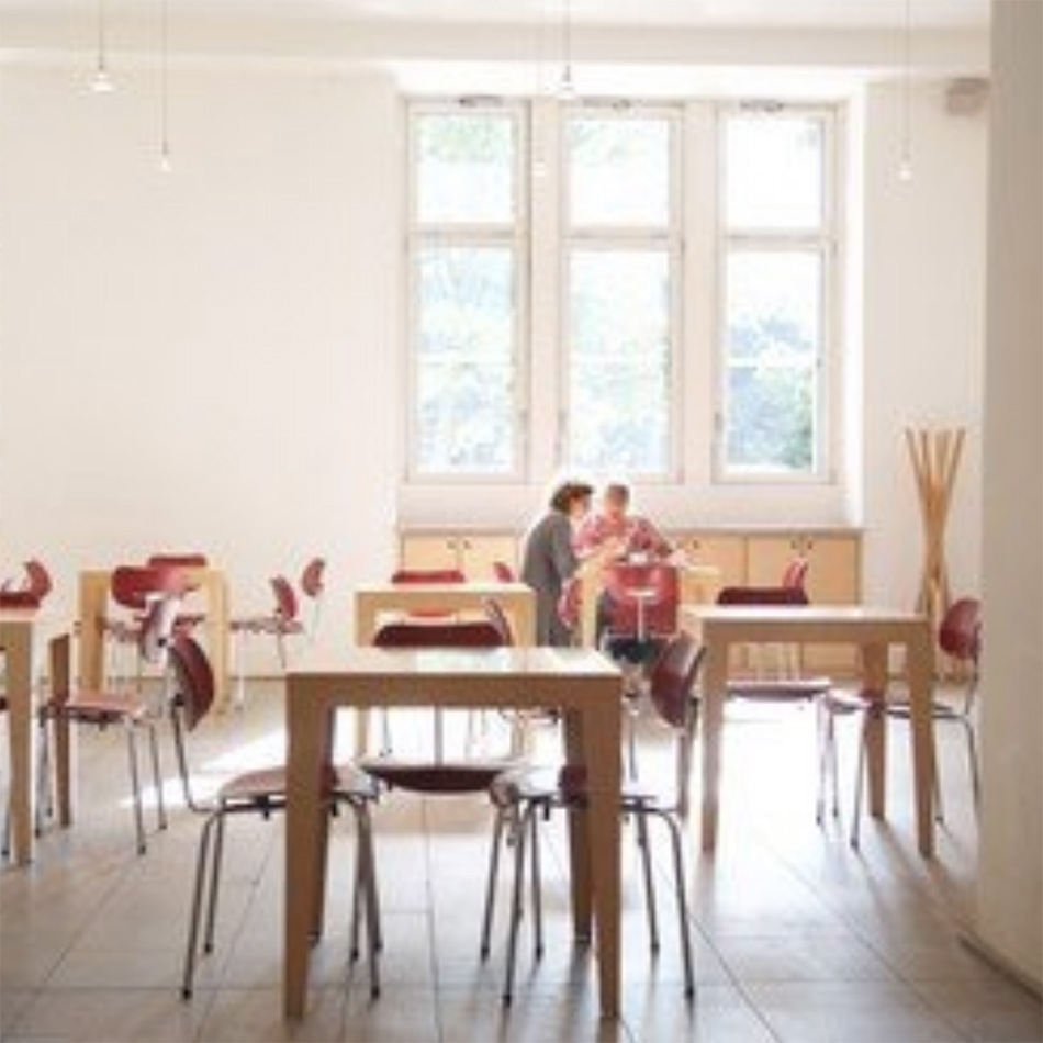 Helle Cafeteria mit Menschen an Tischen sitzend.